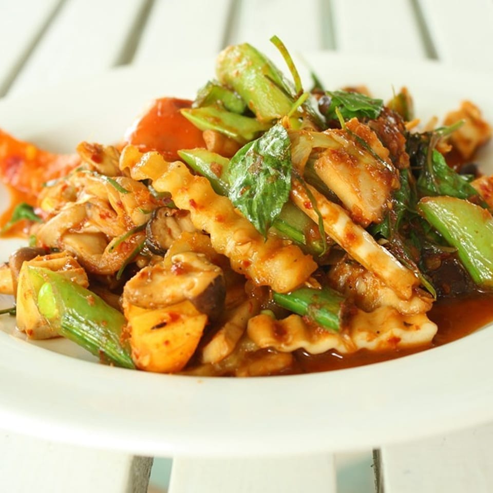 Spicy stir-fried seafood and vegetables with mushrooms, peppers, herbs, and red sauce on a white plate.