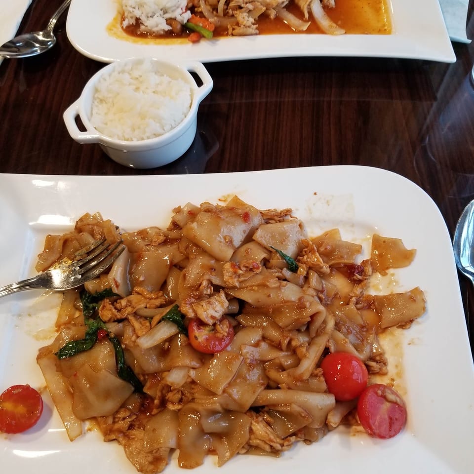 Two plates of Thai food, one with noodles and the other with curry and rice.
